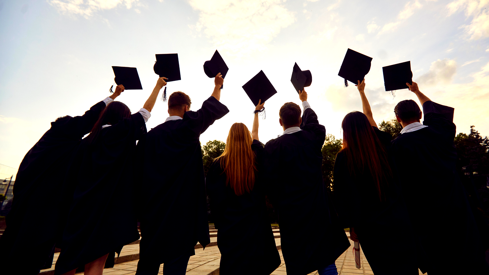 Graduates in gowns raising their caps to the sky. 