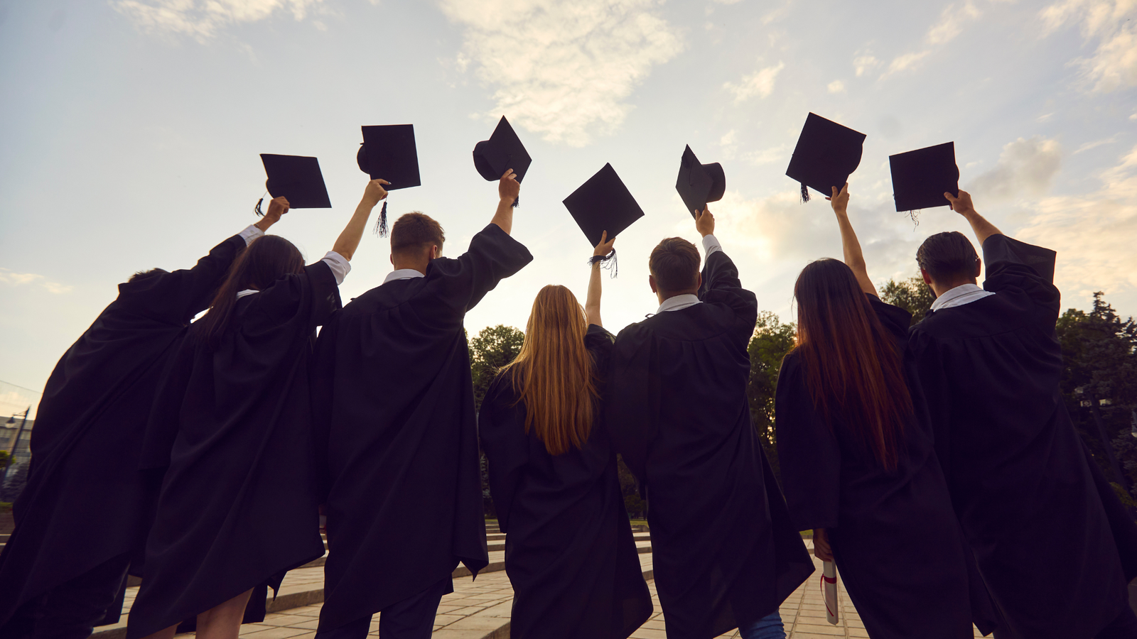 Graduates in gowns raising their caps to the sky. 