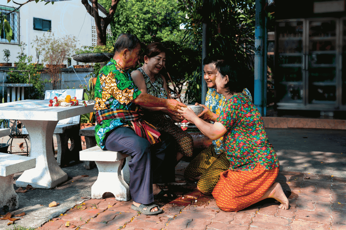 A Thai couple show respect to their elders by kneeling down in front of them and handing them offerings. 